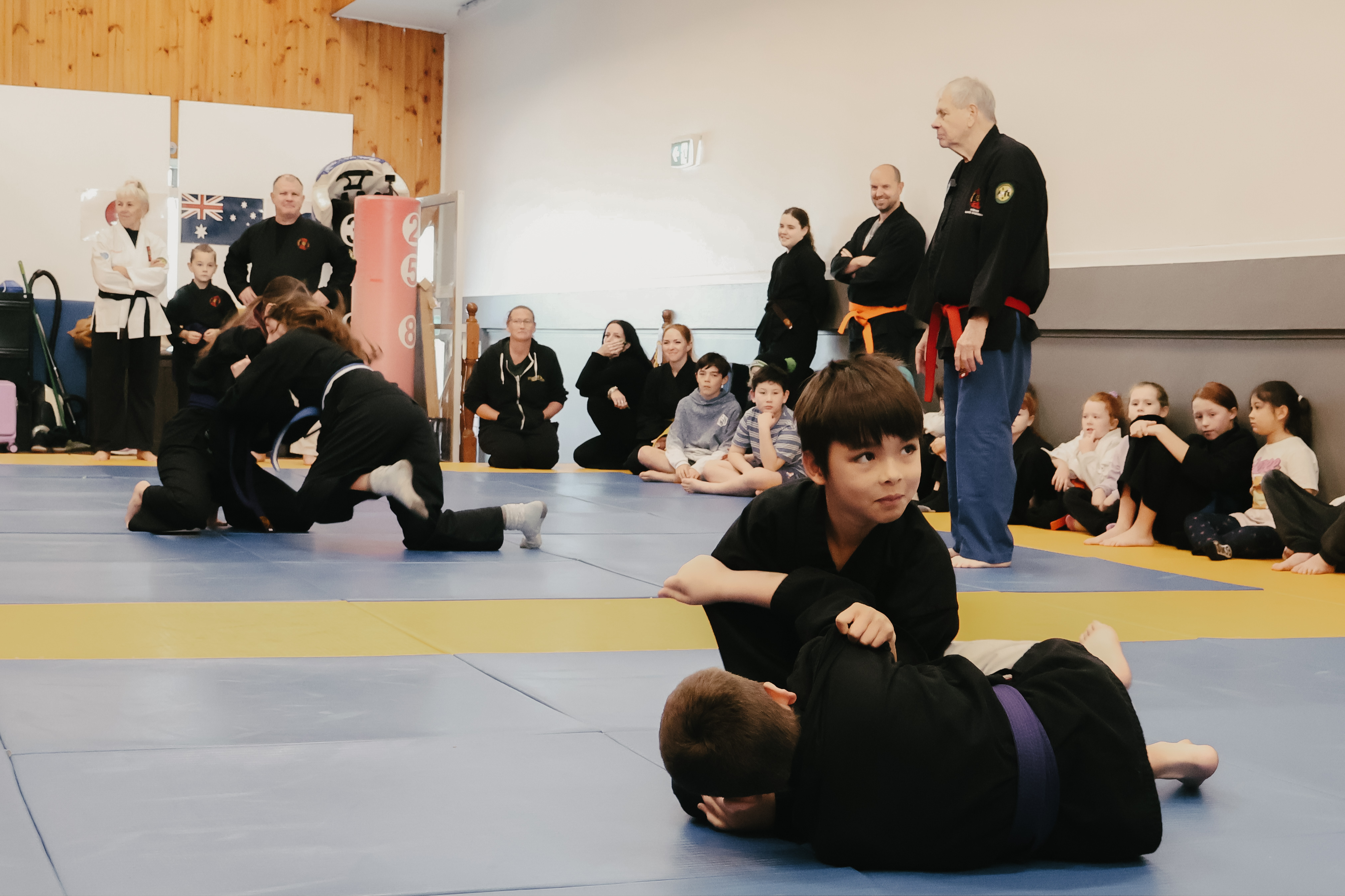 Kids practising ground techniques while classmates watch